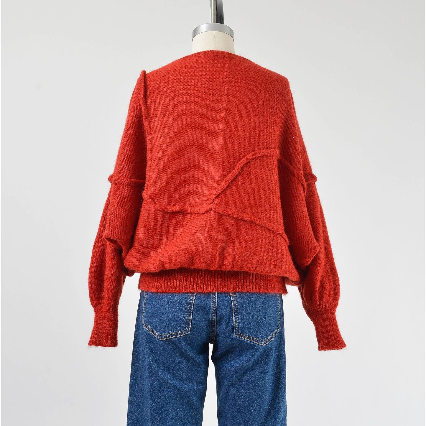 A vintage 1980s red batwing mohair blend knit top with slouchy sleeves and a slit neckline, displayed on a mannequin with a pair of blue jeans.