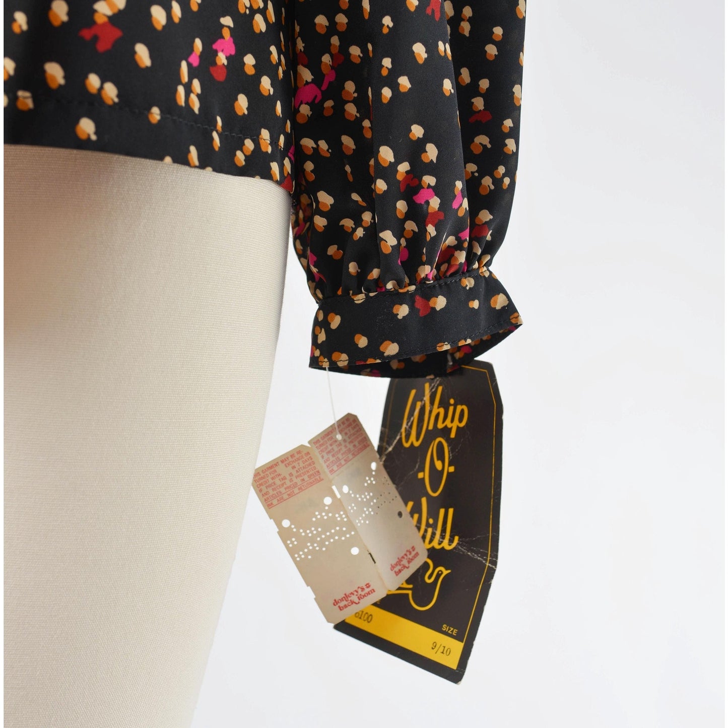 View of hang tags on 70s black spotted blouse. Matte silky fabric. Collared neckline with long puff sleeves.