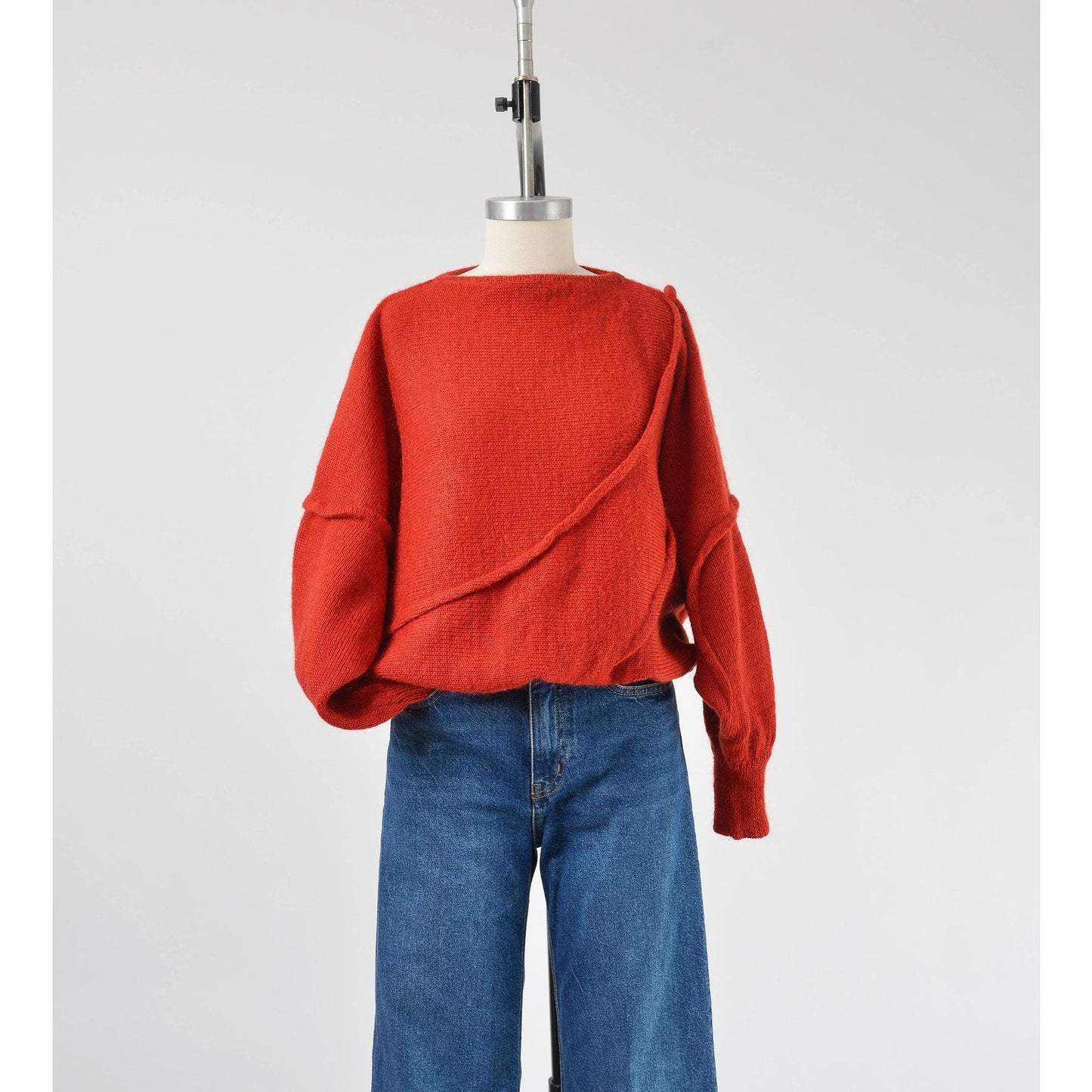 A vintage 1980s red batwing mohair blend knit top with slouchy sleeves and a slit neckline, displayed on a mannequin with a pair of blue jeans.