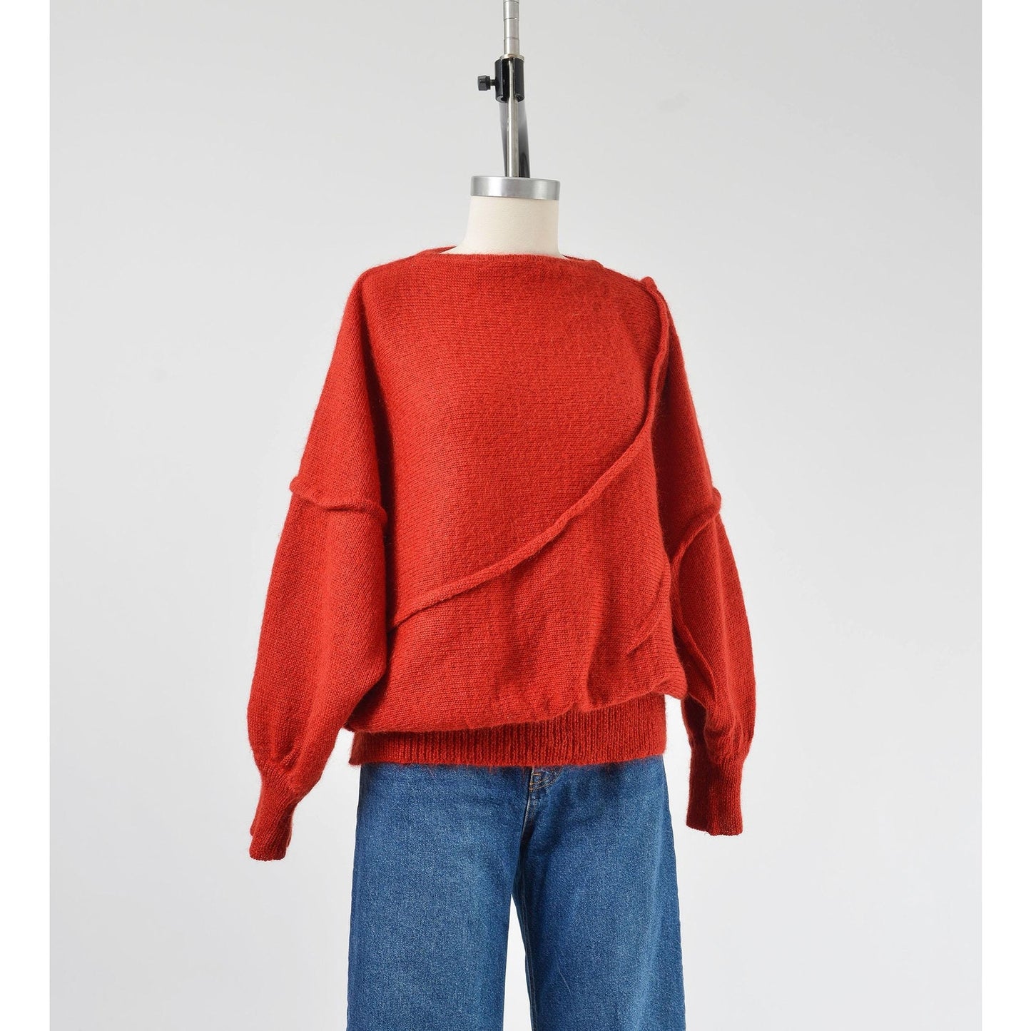 A vintage 1980s red batwing mohair blend knit top with slouchy sleeves and a slit neckline, displayed on a mannequin with a pair of blue jeans.