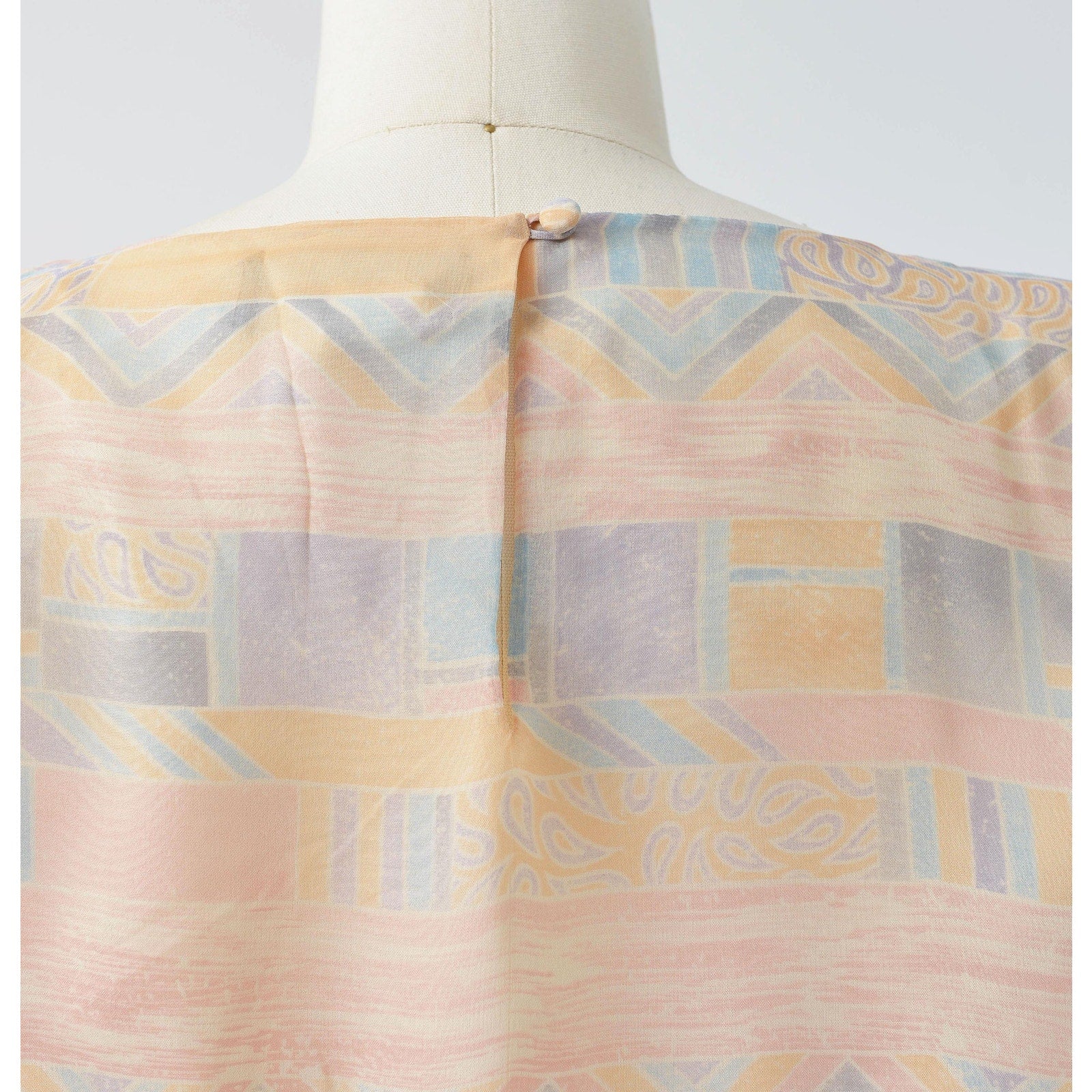 View of rear button closure at back neck on the 70s pastel geometric sheer chiffon blouson midi dress with tie belt. 