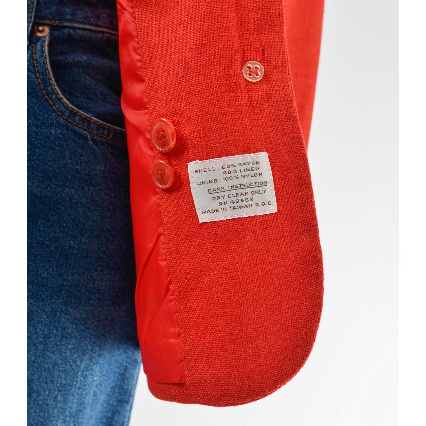 Close-up of a red jacket with a label and blue jeans on a white background