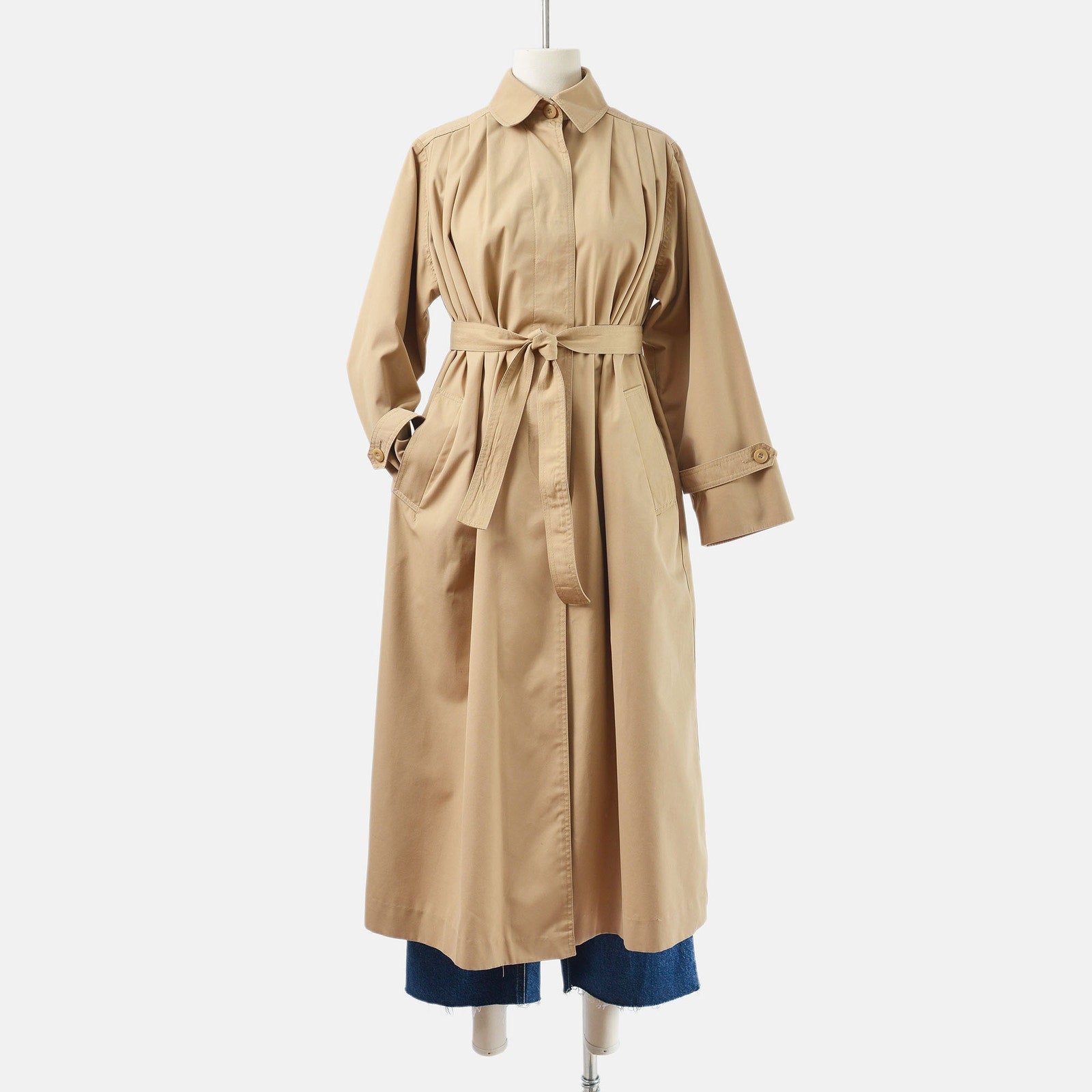 Vintage 70's tan trench coat with tie belt. Full length view with sleeve tucked into the right pocket. 