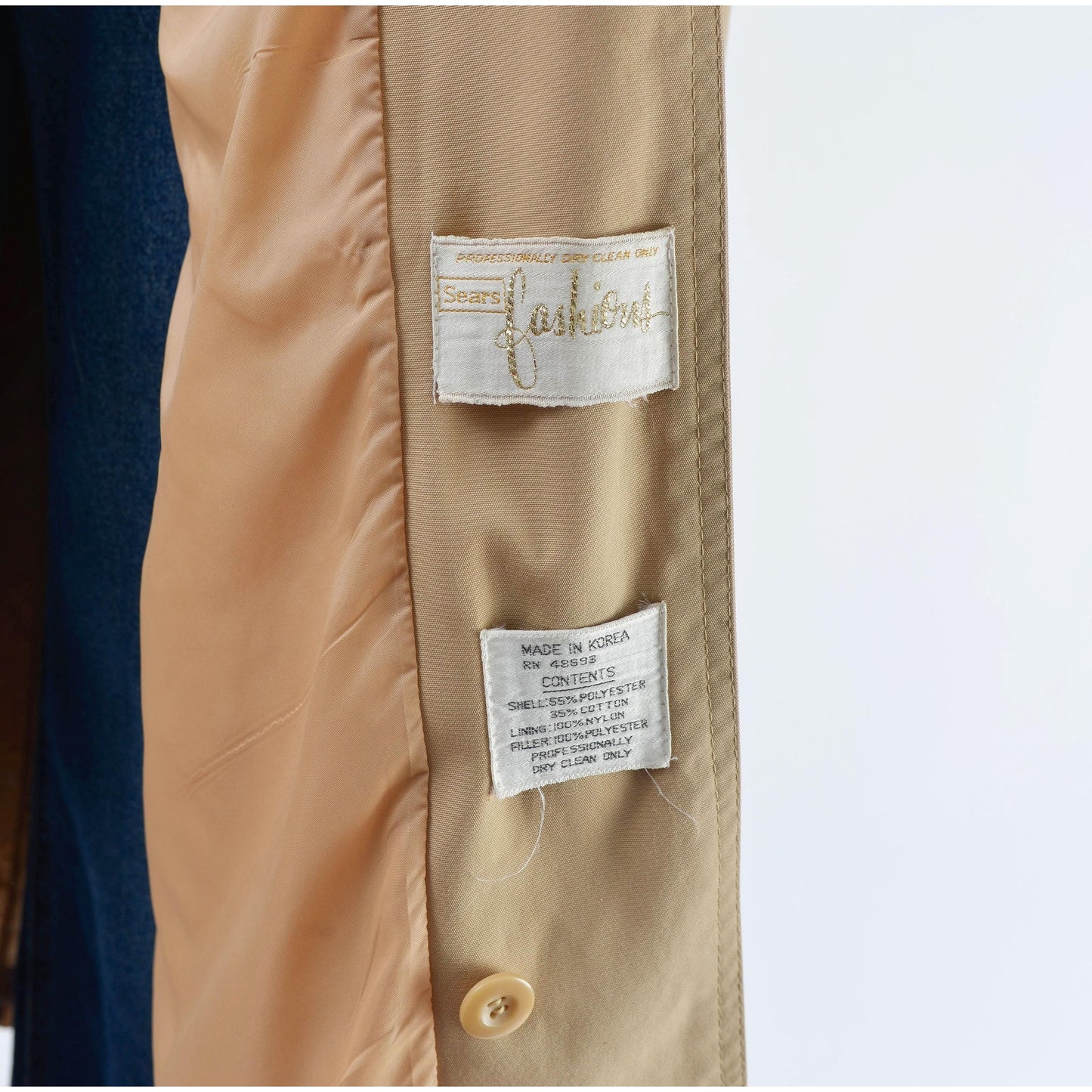 Close-up of a tan trench coat with brand and care label on a white background
