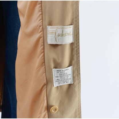 Close-up of a tan trench coat with brand and care label on a white background