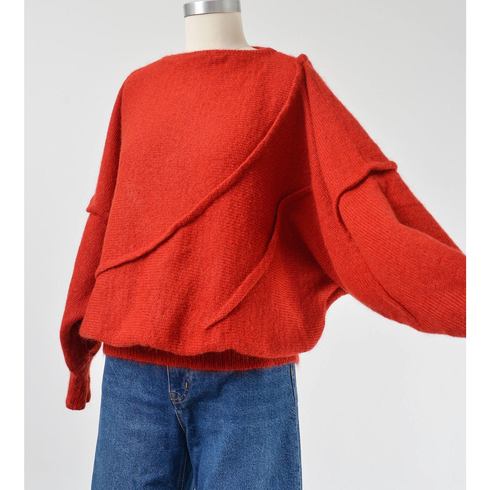 A vintage 1980s red batwing mohair blend knit top with slouchy sleeves and a slit neckline, displayed on a mannequin with a pair of blue jeans.