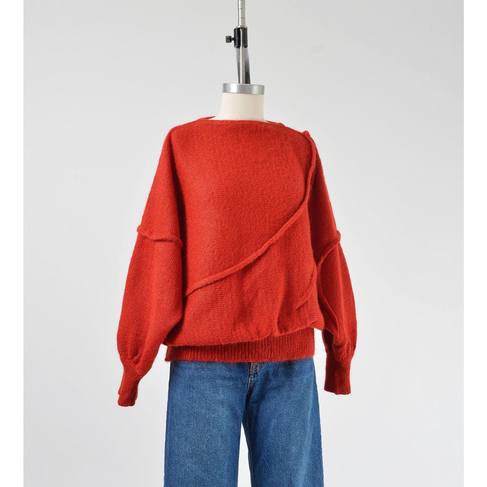 A vintage 1980s red batwing mohair blend knit top with slouchy sleeves and a slit neckline, displayed on a mannequin with a pair of blue jeans.