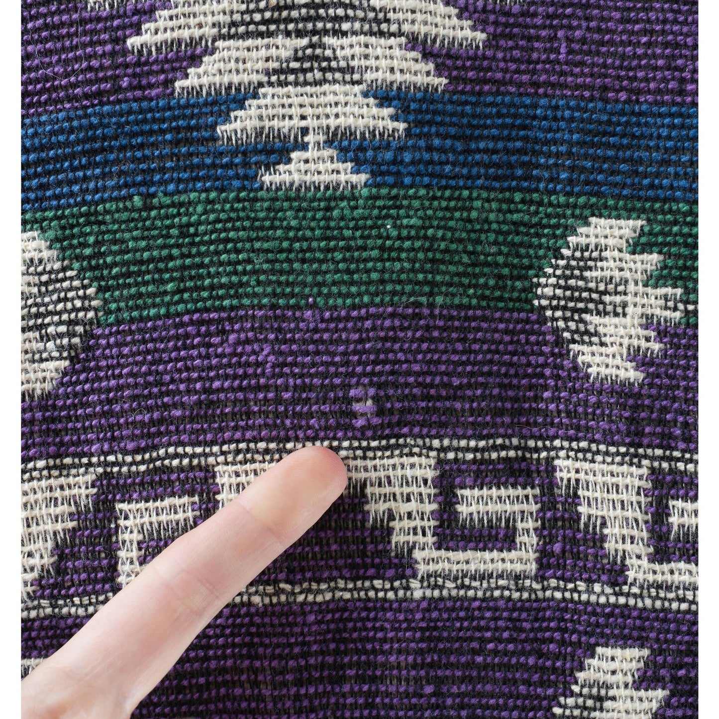 Close-up of a textured fabric with geometric patterns in purple, green, and white.